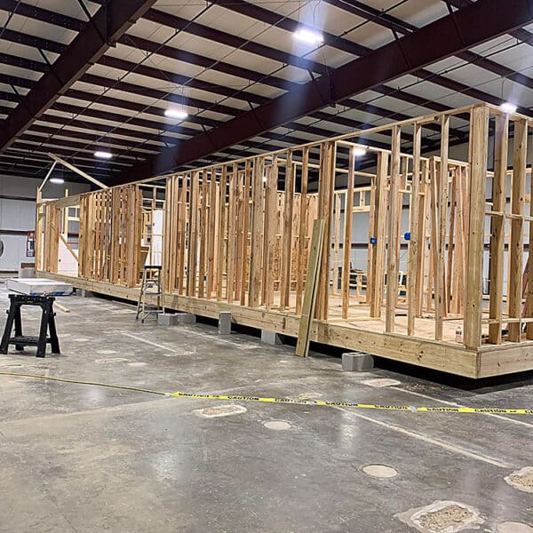 A wooden frame of a prefabricated house under construction inside a large warehouse.